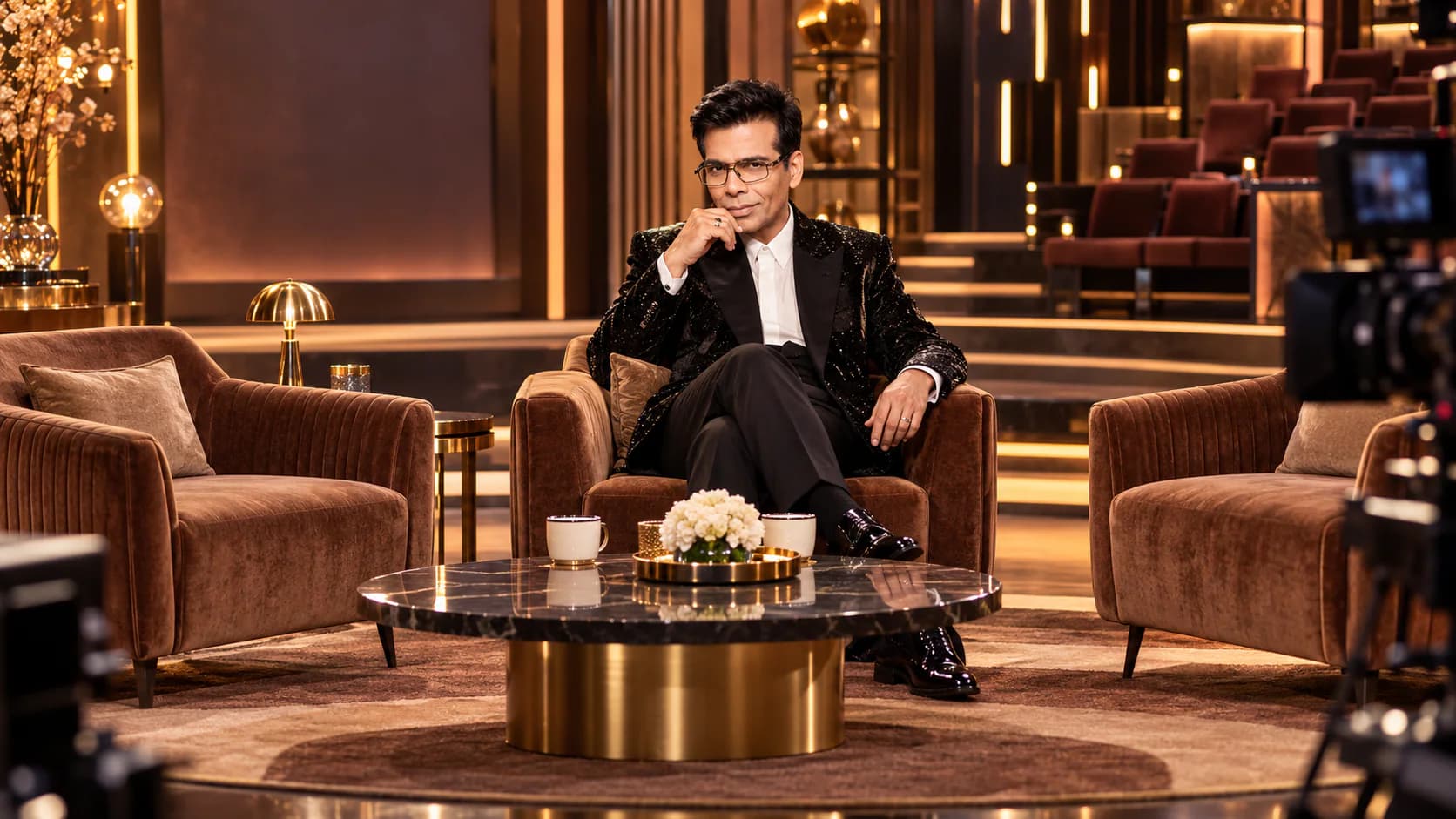 Karan Johar sits on a television talk-show set for the final season of Koffee With Karan.
